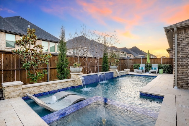 pool at dusk with a hot tub, pool water feature, and a patio area