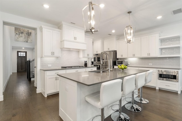 kitchen with white cabinetry, decorative light fixtures, sink, and a center island with sink