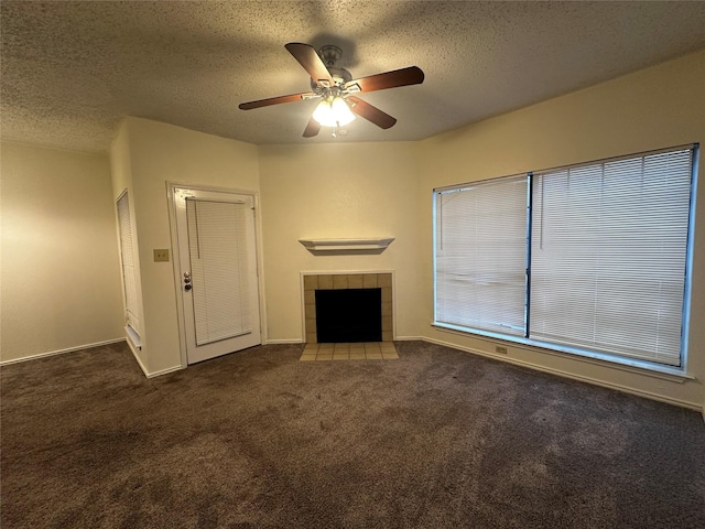 unfurnished living room with a tiled fireplace, ceiling fan, a textured ceiling, and dark colored carpet