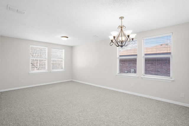 carpeted spare room with an inviting chandelier, plenty of natural light, and a textured ceiling