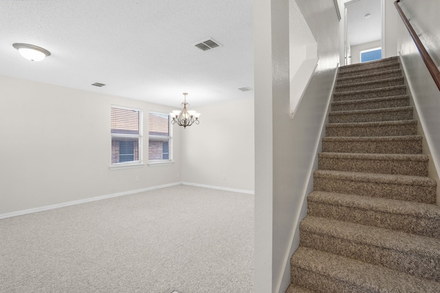 stairway with an inviting chandelier, a textured ceiling, and carpet