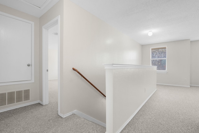 corridor featuring light colored carpet and a textured ceiling