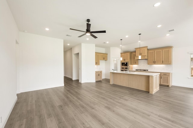 kitchen featuring a sink, stainless steel microwave, recessed lighting, light countertops, and an island with sink