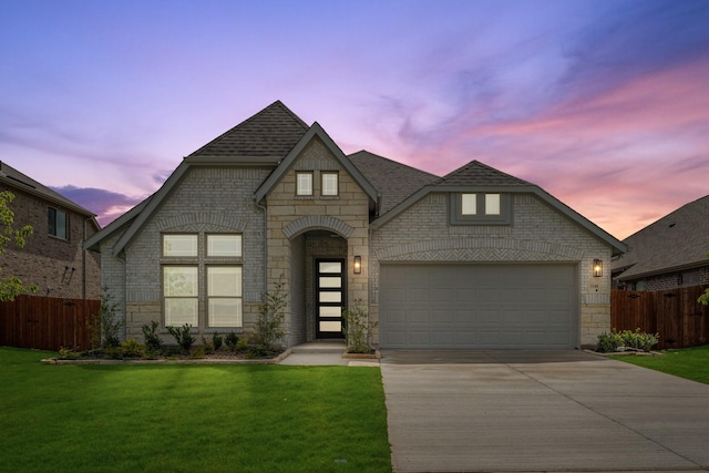 french country inspired facade with driveway, an attached garage, stone siding, a shingled roof, and brick siding