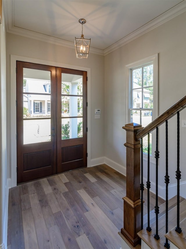 foyer featuring french doors, wood-type flooring, crown molding, and an inviting chandelier