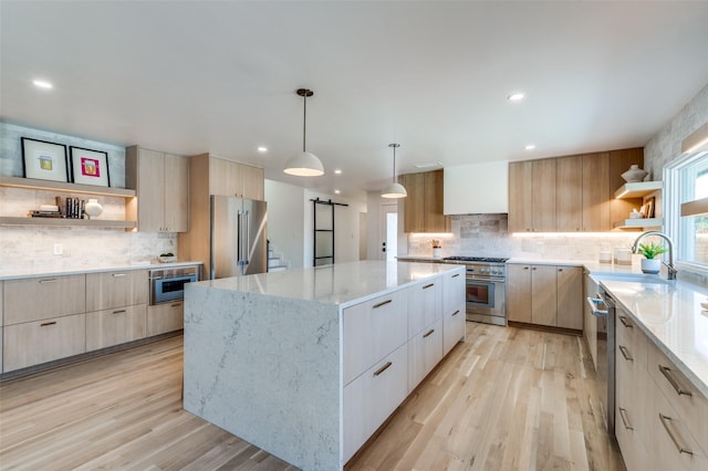 kitchen with sink, high end appliances, decorative light fixtures, a kitchen island, and a barn door