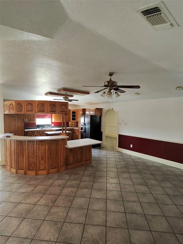 kitchen featuring dark tile patterned floors, black fridge, a textured ceiling, and kitchen peninsula