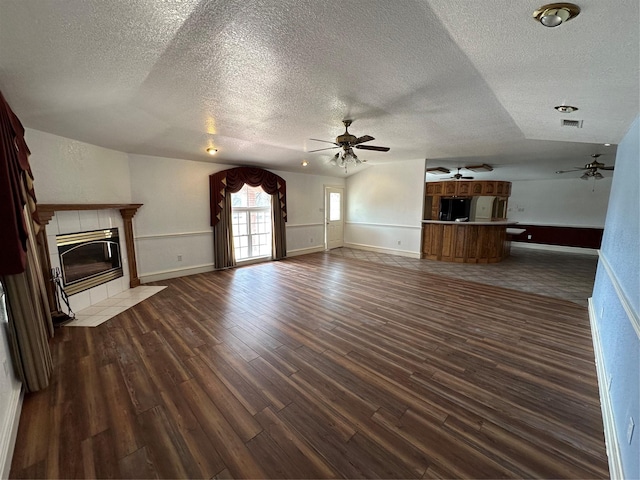 unfurnished living room with vaulted ceiling, a textured ceiling, dark hardwood / wood-style flooring, ceiling fan, and a fireplace