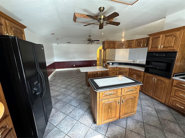 kitchen featuring ceiling fan, black appliances, a center island, and a textured ceiling