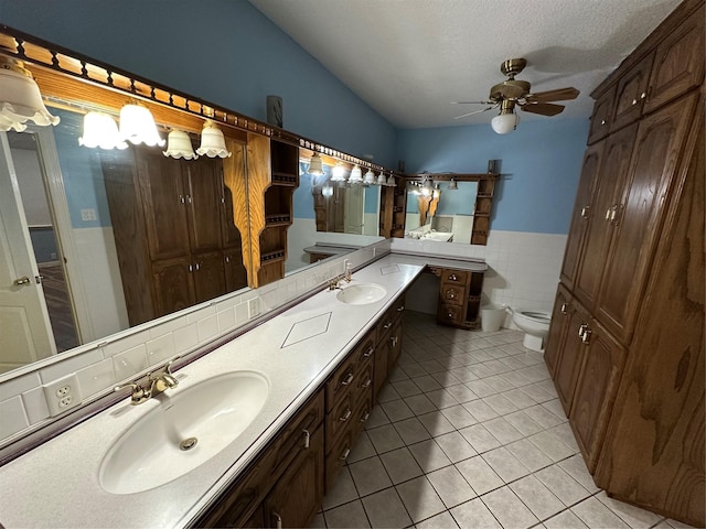 bathroom with ceiling fan, tile patterned flooring, tile walls, vanity, and toilet