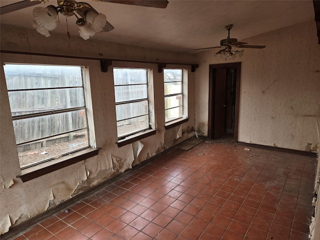 empty room with dark tile patterned flooring, a healthy amount of sunlight, and ceiling fan