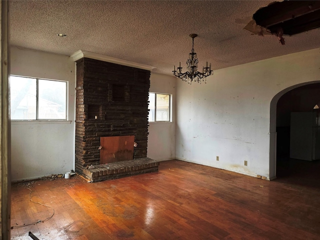 unfurnished living room featuring a notable chandelier, a textured ceiling, a fireplace, and wood-type flooring