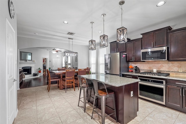 kitchen featuring a breakfast bar area, appliances with stainless steel finishes, decorative backsplash, a kitchen island, and decorative light fixtures