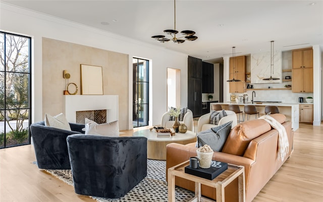 living room featuring sink, light hardwood / wood-style flooring, a premium fireplace, an inviting chandelier, and ornamental molding