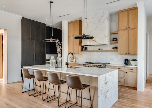 kitchen featuring hanging light fixtures, decorative backsplash, an island with sink, and light wood-type flooring