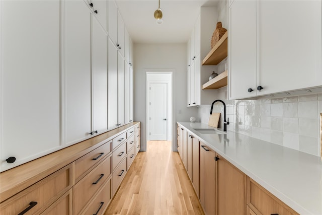 kitchen featuring white cabinetry, sink, light hardwood / wood-style flooring, and backsplash