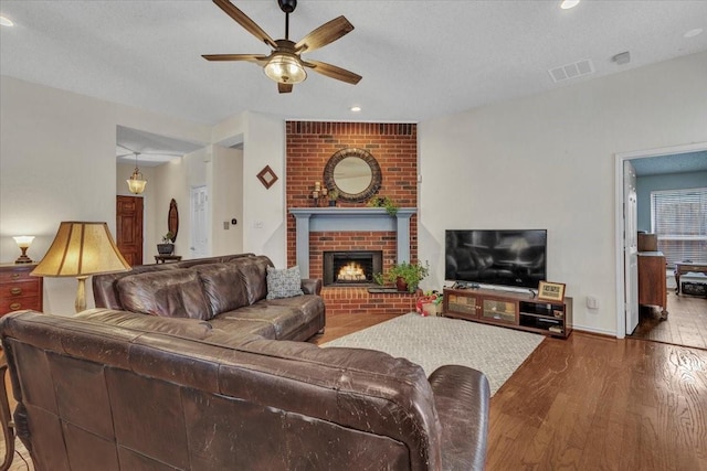 living room featuring hardwood / wood-style flooring, ceiling fan, a fireplace, and a textured ceiling