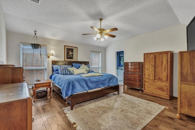 bedroom with lofted ceiling, ceiling fan, hardwood / wood-style floors, ensuite bathroom, and a textured ceiling