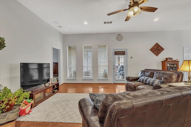 living room featuring ceiling fan, light hardwood / wood-style flooring, and a textured ceiling