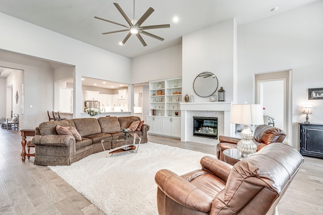 living room with ceiling fan, light hardwood / wood-style floors, built in features, and a high ceiling