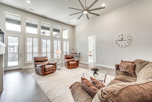 living room with a towering ceiling, hardwood / wood-style floors, and ceiling fan