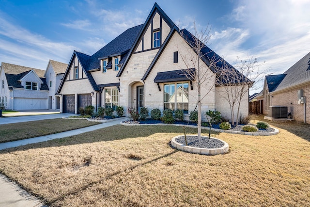 english style home with a garage, a front lawn, and central air condition unit