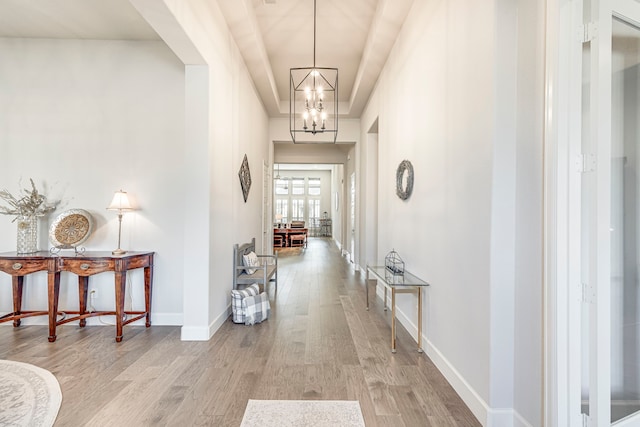 hall featuring a raised ceiling, light hardwood / wood-style floors, and a notable chandelier