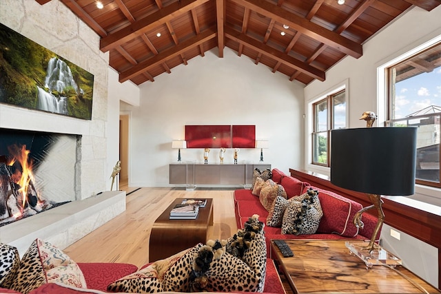 living room featuring a stone fireplace, light hardwood / wood-style flooring, high vaulted ceiling, and beamed ceiling