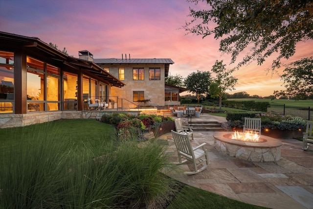 back house at dusk featuring a patio, a yard, and a fire pit