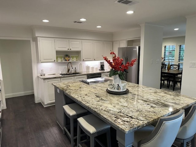 kitchen with a breakfast bar, light stone counters, freestanding refrigerator, visible vents, and a sink
