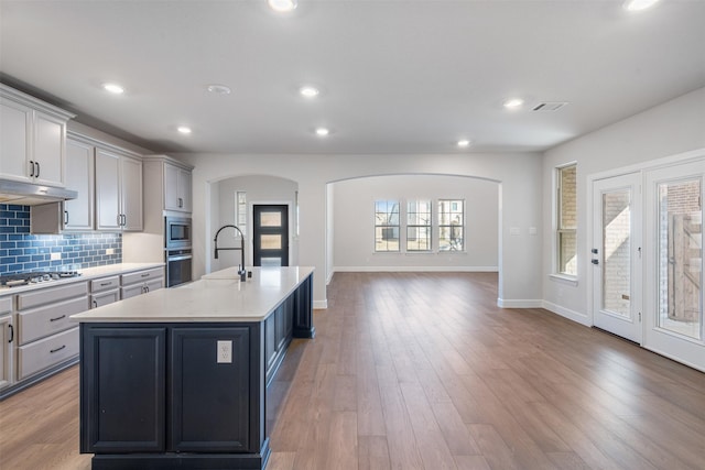 kitchen featuring sink, a center island with sink, gray cabinets, and appliances with stainless steel finishes