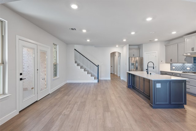 kitchen with light hardwood / wood-style flooring, stainless steel fridge, tasteful backsplash, and a center island with sink