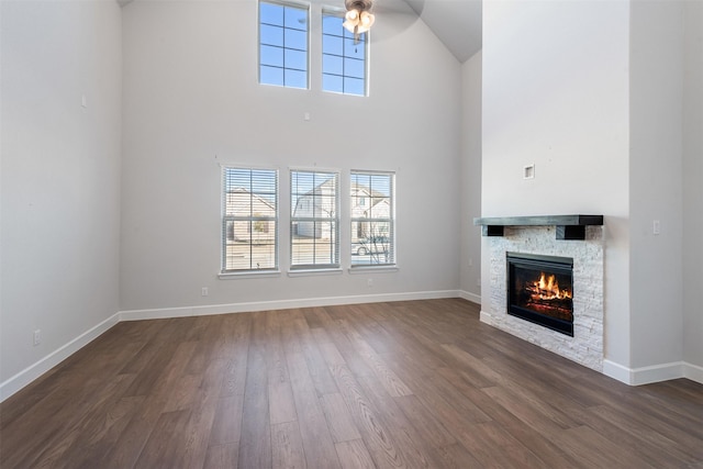 unfurnished living room with a towering ceiling, a stone fireplace, and dark hardwood / wood-style flooring