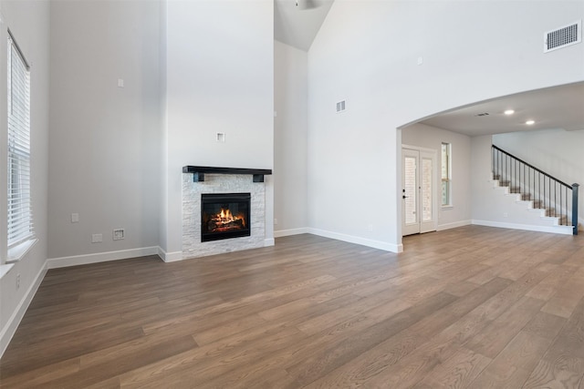 unfurnished living room with hardwood / wood-style flooring, a stone fireplace, and a towering ceiling