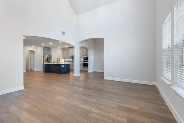 unfurnished living room with hardwood / wood-style floors, a towering ceiling, and sink