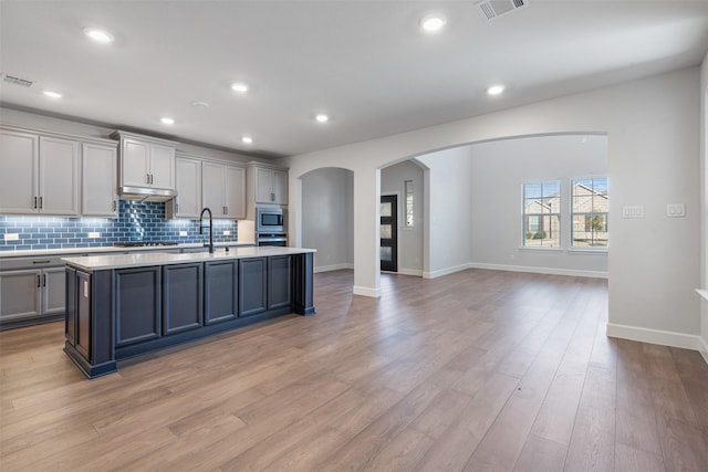 kitchen featuring gray cabinetry, tasteful backsplash, a kitchen island with sink, stainless steel appliances, and light hardwood / wood-style floors