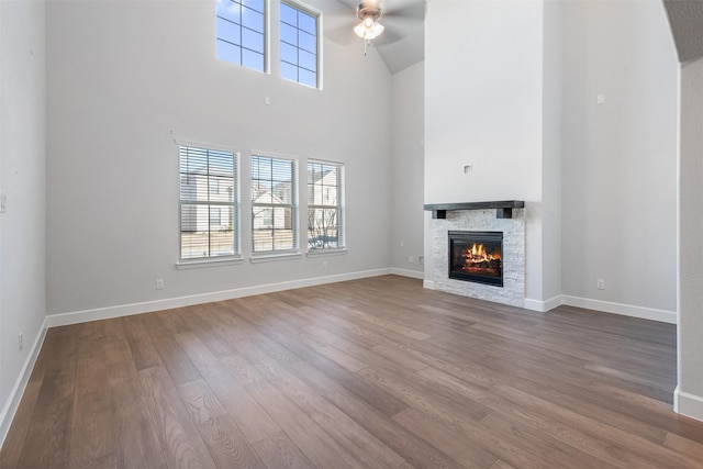 unfurnished living room featuring hardwood / wood-style flooring, ceiling fan, a stone fireplace, and a high ceiling