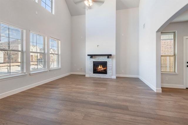 unfurnished living room featuring hardwood / wood-style flooring, a fireplace, ceiling fan, and a high ceiling