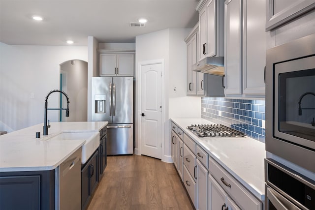 kitchen featuring an island with sink, sink, gray cabinetry, light stone counters, and stainless steel appliances