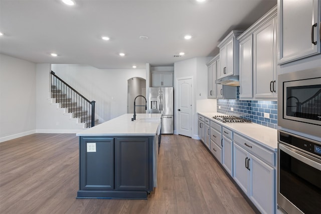 kitchen featuring an island with sink, appliances with stainless steel finishes, dark wood-type flooring, and gray cabinetry