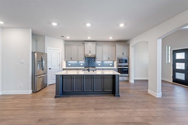 kitchen with appliances with stainless steel finishes, a kitchen island with sink, decorative backsplash, and light hardwood / wood-style flooring