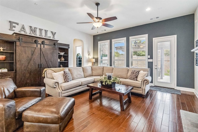 living room with dark hardwood / wood-style flooring, ceiling fan, and a barn door