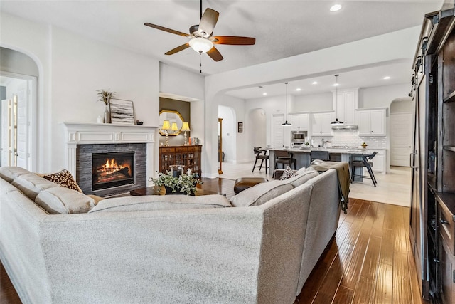 living room featuring a stone fireplace, wood-type flooring, and ceiling fan