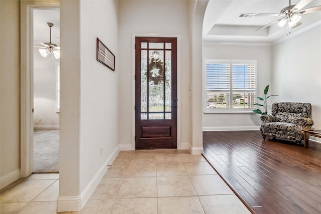 tiled entrance foyer with ceiling fan, ornamental molding, and a raised ceiling