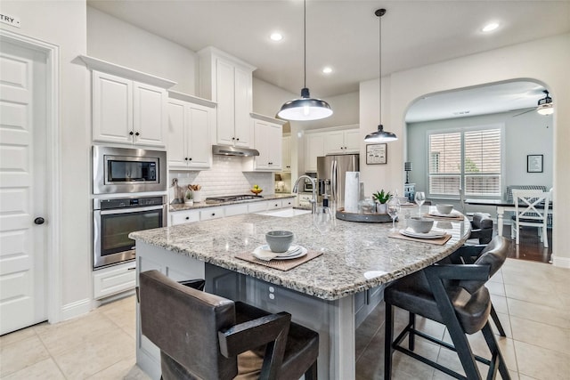 kitchen with white cabinetry, an island with sink, stainless steel appliances, sink, and a kitchen bar