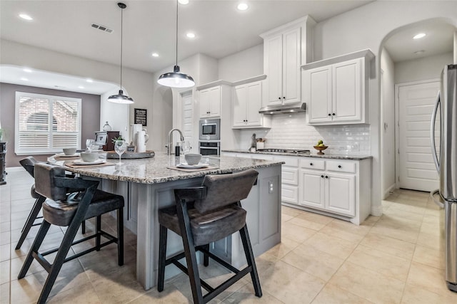 kitchen with stainless steel appliances, white cabinetry, an island with sink, and light stone counters