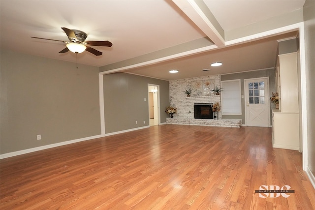 unfurnished living room with beamed ceiling, ceiling fan, a fireplace, and light wood-type flooring