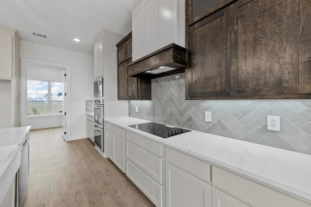 kitchen featuring light stone counters, stainless steel oven, tasteful backsplash, black electric stovetop, and white cabinets