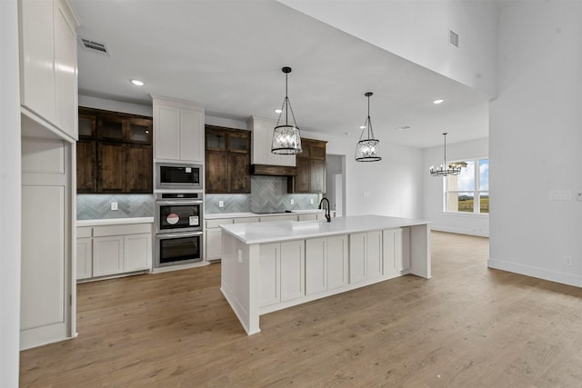 kitchen featuring black electric cooktop, dark brown cabinetry, an island with sink, built in microwave, and decorative backsplash