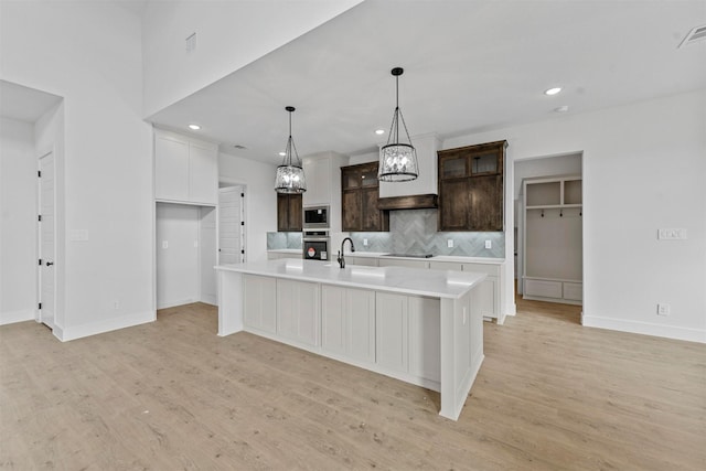 kitchen with appliances with stainless steel finishes, backsplash, dark brown cabinetry, an island with sink, and light wood-type flooring